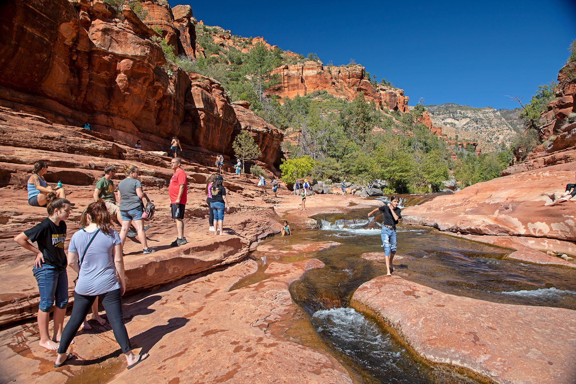 People walking along the creek with red rocks in background